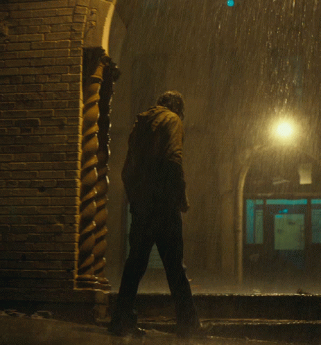 man walking down street at night under falling rain