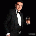 a man in a tuxedo holding up a small wine glass