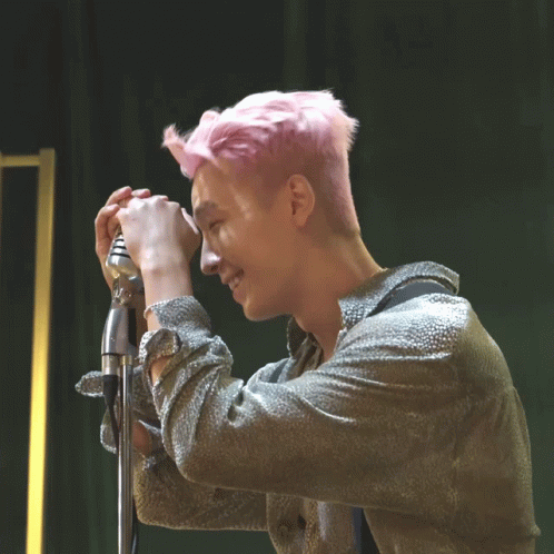 the man with pink hair has his hands behind his ears