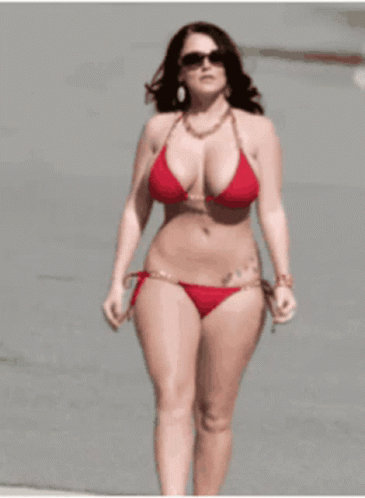 a woman with glasses and a bathing suit walking along the beach