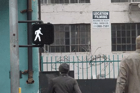 two men walking in the street towards a sign with locations and a picture of a person coming up from the back