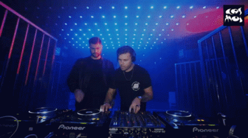 two men stand beside each other and turn records on some decks
