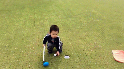 small boy kneeling down on the ground putting a ball in his hands
