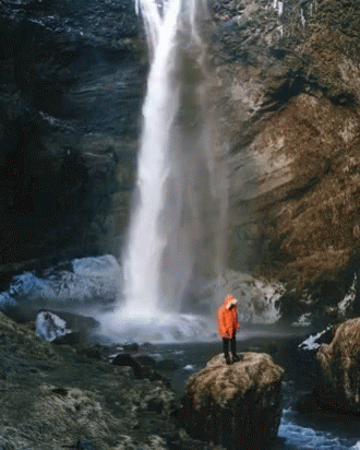 the man stands at the base of a waterfall