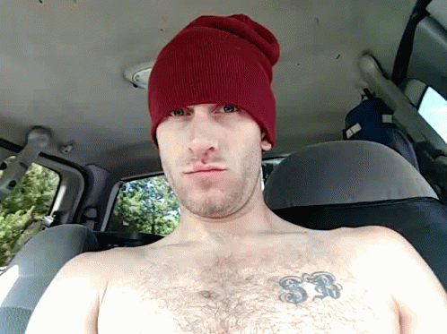 a shirtless man with a blue hat is seen through the rear seat