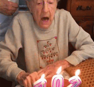 a woman is sitting in front of her birthday cake with lit candles on it