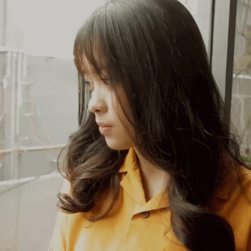 a girl with long black hair standing next to a window
