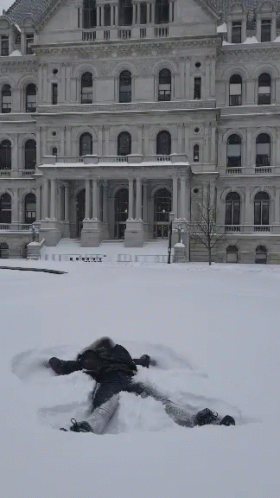 person lying in the snow in front of a large building