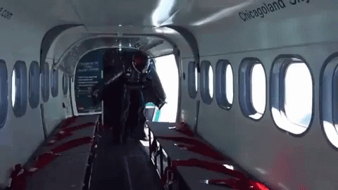 a man in a full body wetsuit walking on an airplane aisle