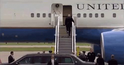 president bush walks into an airplane while being escorted by his entourage
