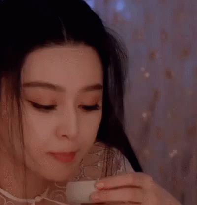 a young asian girl with her eyes closed is holding a coffee cup and has her eyes open