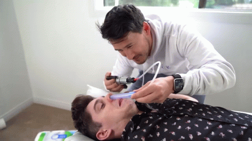 man getting facial haircut from a man on a hospital bed