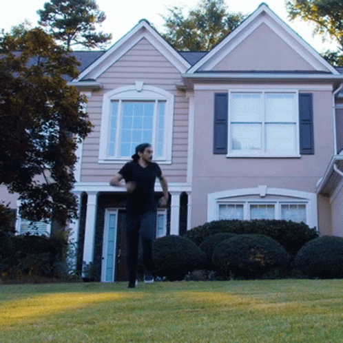 a house in the background is painted gray with lots of windows and has a man standing by the front door