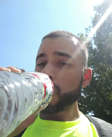a man in a green shirt drinks from a plastic water bottle