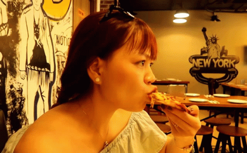 a woman with short hair eats a slice of pizza