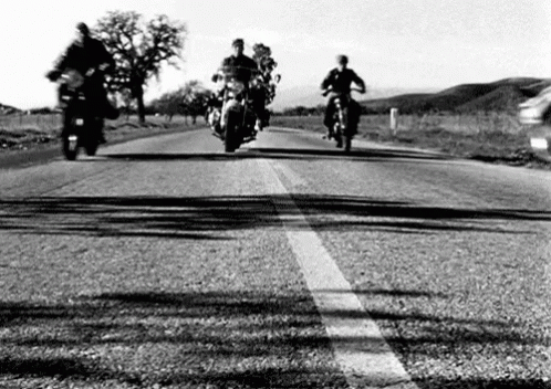three men riding motorcycles down a road on a sunny day