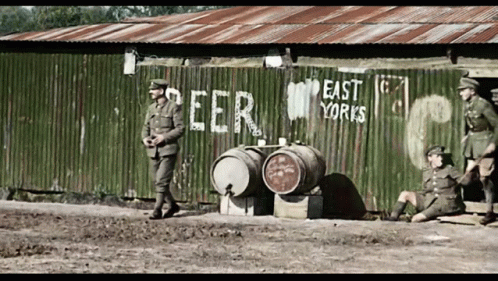 soldiers are standing near a shed that has beer barrels in front