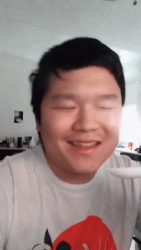 an asian man smiling for the camera with his eyes closed