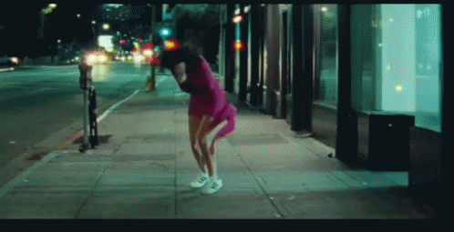 a woman is dancing down the sidewalk at night