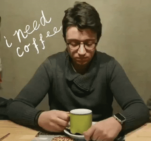 a man in a black sweater sits at a table with a book and mug