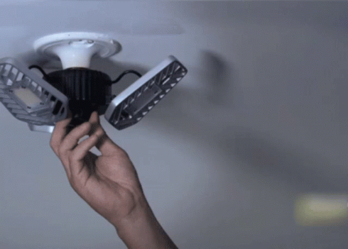 a hand is holding a remote control and three ceiling fan blades