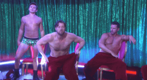 the three shirtless men are standing and sitting in a row