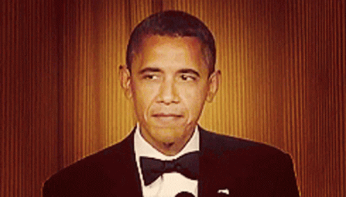 obama is dressed in a tuxedo, standing in front of blue light