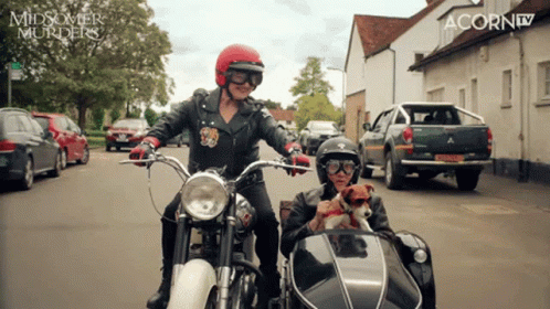 two people on motorcycles in front of a row of parked cars