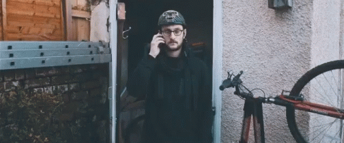 a man with a hat talking on a phone while standing outside of a house