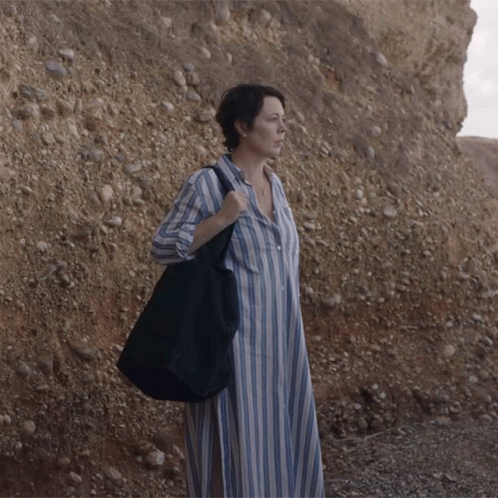 a woman with a bag standing against a rock