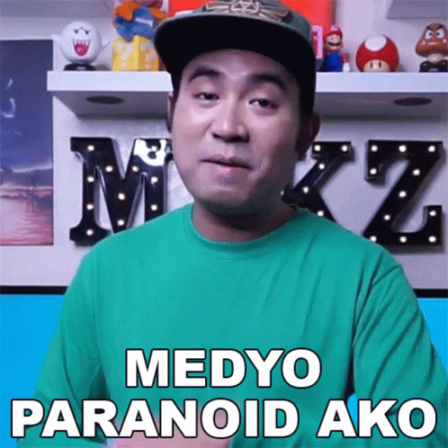 a man with a green shirt and black cap, in front of a sign that says medyo paranoidi ako