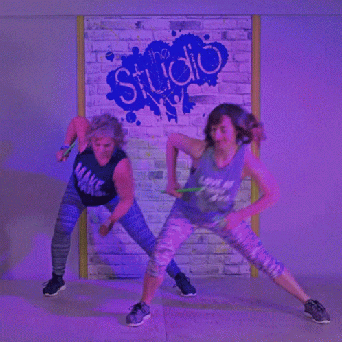 two s are dancing and playing with the neon lights in front of a brick wall