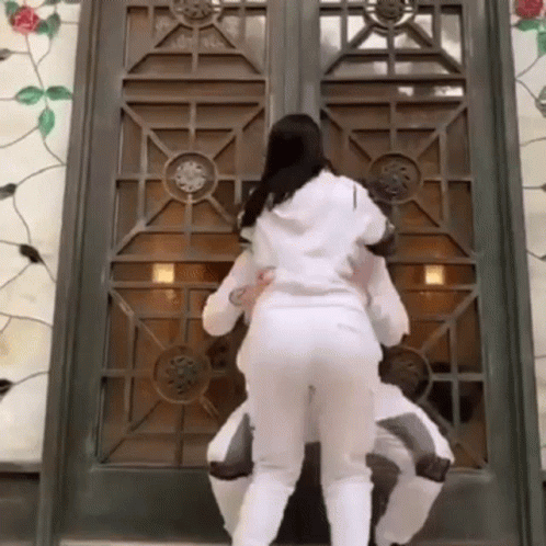 two women in white outfits looking out through a door
