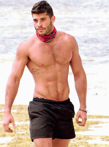 a man without a shirt walking on the beach