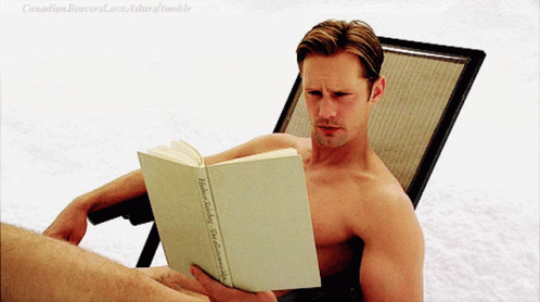 man reading book while sitting on lounge chair outside