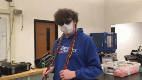 a young man with long hair and a mask stands in a lab