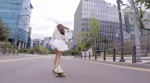 a woman riding a skateboard down a street next to tall buildings