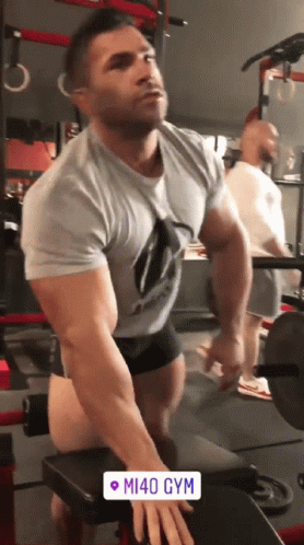 a man lifts a barbell with one hand as another stands behind him
