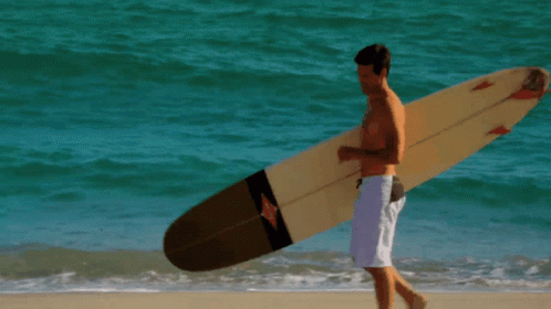 a man walking along the beach with a surfboard