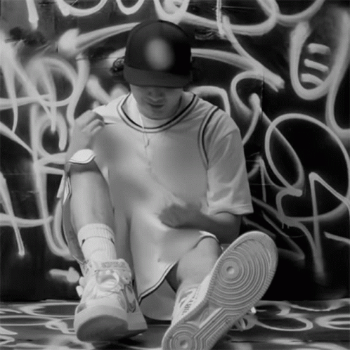 a young man sits against a wall with graffiti