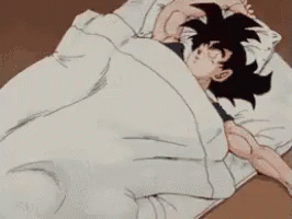 a  with black hair and big eyes, is under the covers of a blanket while his hand is holding his head out in a pillow