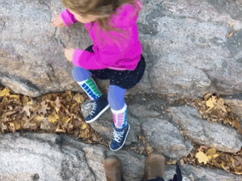 a girl jumping up on top of a rocky slope
