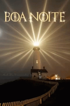 light beams shine through the night sky as a lighthouse sits near a fence