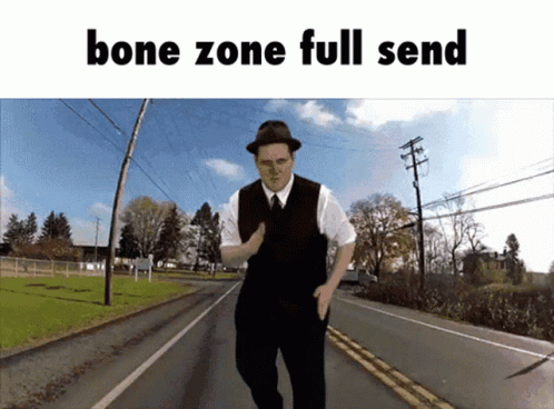 a man in a vest and hat standing on a road with a banner that says bones zone full send