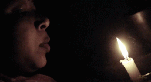 a person standing in the dark holding a lit candle in their hand