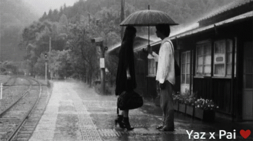 a woman and man standing on a rain soaked train platform with an umbrella