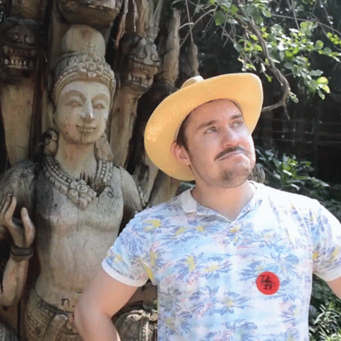 a man wearing a blue hat is posing next to a statue