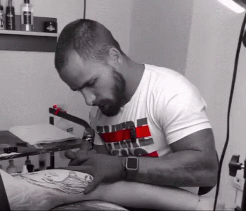 a bearded man is working on a tattoo in his room