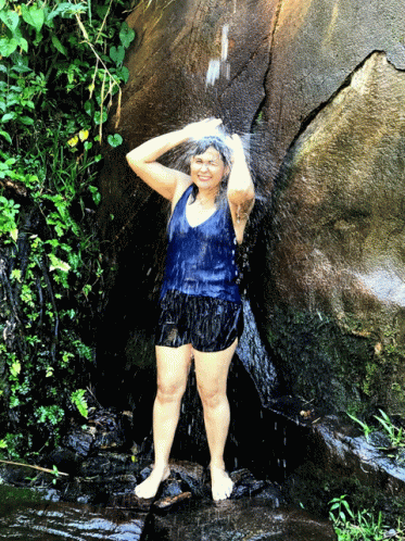 a girl stands next to a waterfall covered in water