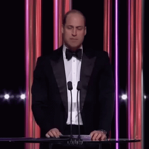 a man in a tuxedo standing behind a microphone at an award show